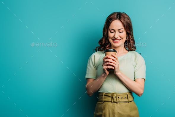 happy girl smiling while holding coffee to go on blue background - Stock Photo - Images