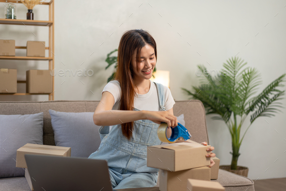 Young entrepreneur is packing clothes into cardboard boxes and using tape to seal for home delivery