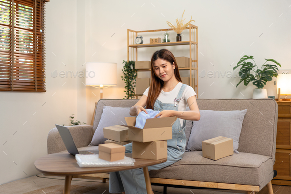 Young entrepreneur is packing clothes into cardboard boxes for home delivery to customers while