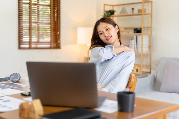Female freelance is feeling pain in shoulder and back while reading business report on laptop