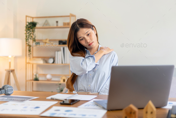 Female freelance is feeling pain in shoulder and back while reading business report on laptop