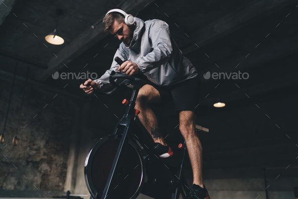 Man in headphones exercising on spinning cycle in gym