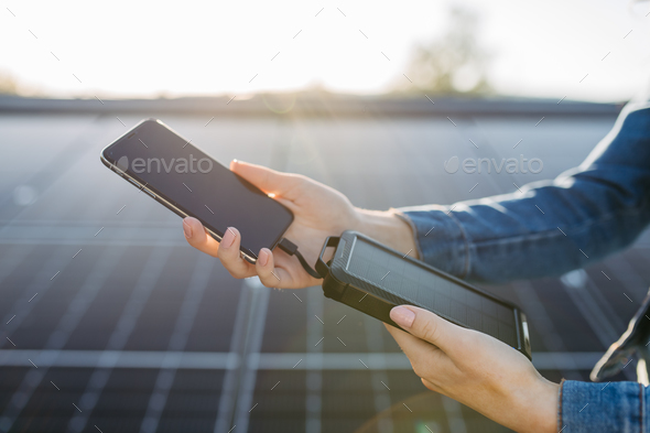 Close up of woman charging her phone with solar charger on the roof with photovoltaics panels.