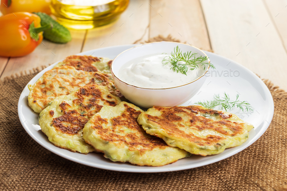 Vegan zucchini pancakes in plate and cream sauce on wooden background. Healthy vegan diet food. - Stock Photo - Images