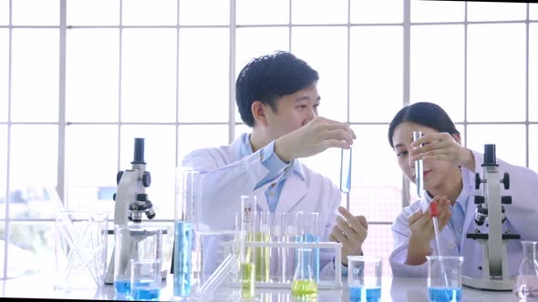 Young Asian Female Scientist Doing Research in Laboratory Wearing Lab Coat and Gloves with Colleague alt