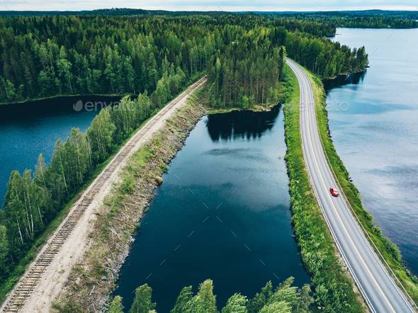 Aerial view of road with red car and train line railway over blue lake water in Finland - Stock Photo - Images