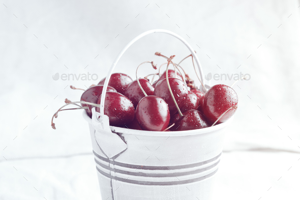 Small white bucket full of red cherries on a light background. Bright sunlight. - Stock Photo - Images