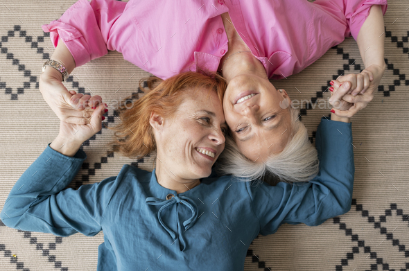 two mature women lying upside down on carpet looking at camera,