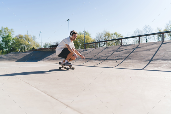 Skateboarder in headphones squatting on skateboard
