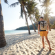 Tourist with backpack walking on beautiful beach with palm trees at sunset - PhotoDune Item for Sale