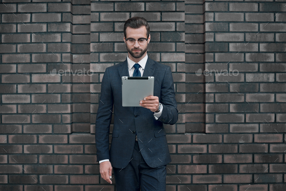 A young businessman in glasses and an expensive suit, holds a tablet in his hands - Stock Photo - Images