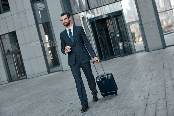 A young businessman spectacled crosses road with coffe and suitcase - Stock Photo - Images