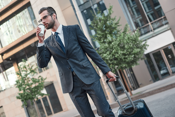 A young businessman spectacled crosses road with coffe and suitcase - Stock Photo - Images