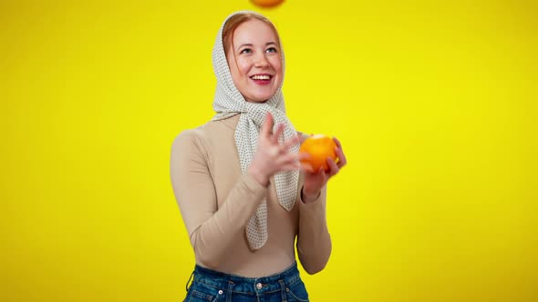 Slim Joyful Redhead Woman Juggling Oranges at Yellow Background alt