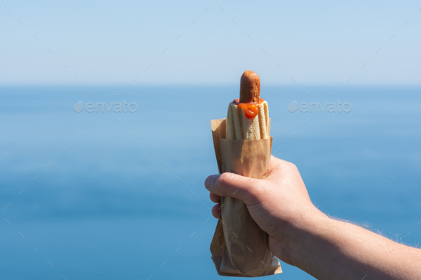 Hot dog in hand against the sky. Fast food. Snack on the street. - Stock Photo - Images