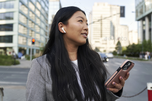 Business Chinese woman wearing earphones and calling on the street - Stock Photo - Images