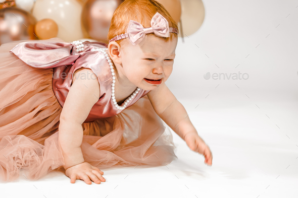 Little crying unhappy redhead baby girl celebrates first birthday anniversary. 1 year family party  - Stock Photo - Images