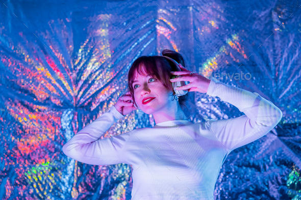 Relaxed smiling woman in white clothes, headphones dancing in neon light. White party. Silent disco.