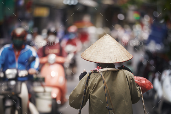 Person with traditional conical hat against traffic motorbikes on busy street - Stock Photo - Images