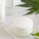 White cream jar with a blank lid near cannabis sativa leaves. Cosmetic Mockup - PhotoDune Item for Sale