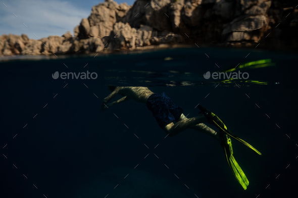 Unrecognizable man swimming underwater in mountainous bay - Stock Photo - Images