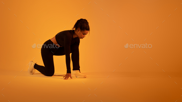 Sport motivation. Determined black sportswoman ready for race posing in crouch start position on