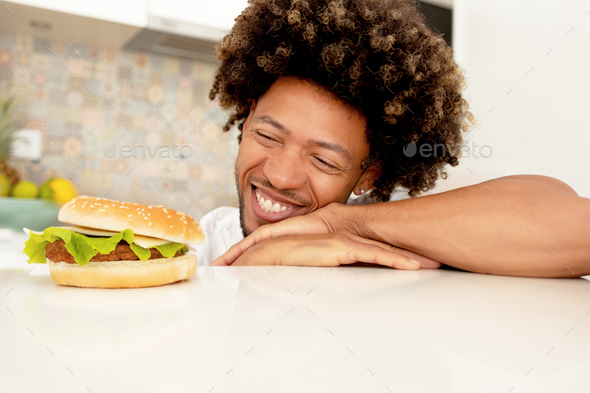 Happy African Guy Looking At Burger On Kitchen Countertop Indoor