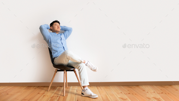 Calm asian mature man relaxing sitting on chair, leaning back holding hands behind head and smiling - Stock Photo - Images