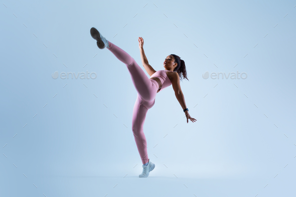Fit black lady raising leg and showing perfect stretching, doing karate side kick over blue - Stock Photo - Images