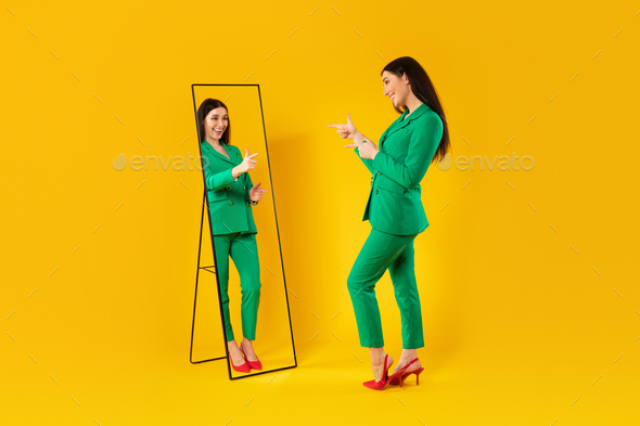 Trendy lady pointing at her reflection in mirror posing after successful shopping, wearing green - Stock Photo - Images