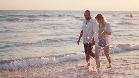 Couple of Young Lovers Holding Hands Walking Along the Beach By the Sea