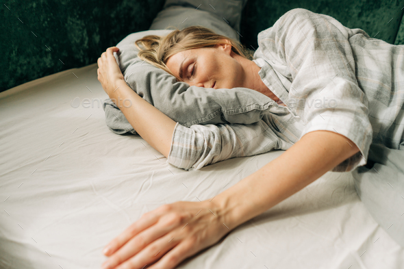 Serene lazy woman sleeping in the morning ignoring the alarm clock not wanting to get out of bed. - Stock Photo - Images