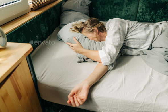 Early in the morning, a woman hides her face in a pillow and is too lazy to get out of bed. - Stock Photo - Images