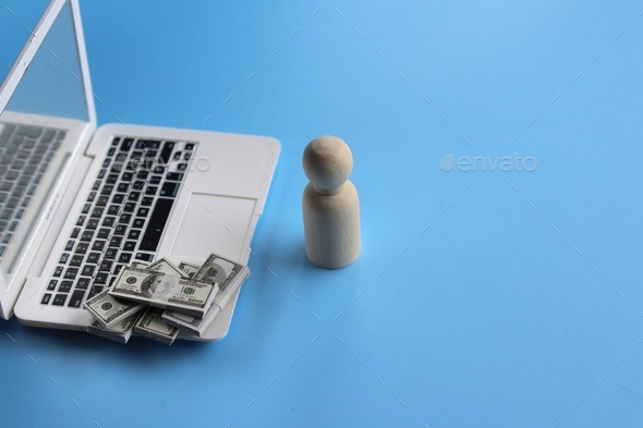 Wooden doll in front of laptop and pile of money.