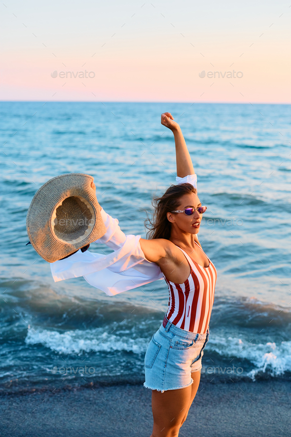 Young woman with raised arms on the beach at sunset. - Stock Photo - Images