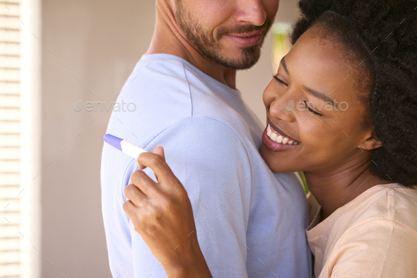 Hugging Multi-Racial Couple In Bedroom At Home Celebrating Positive Pregnancy Test Result - Stock Photo - Images