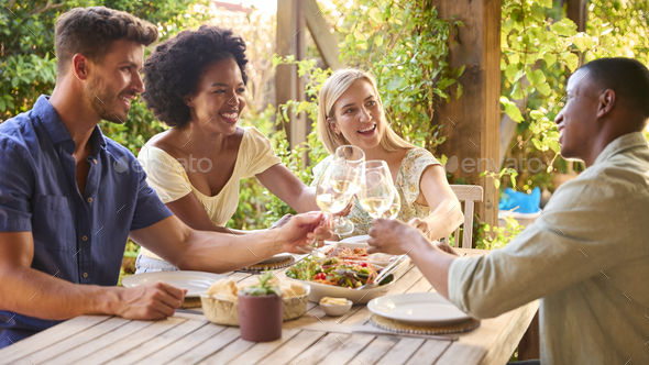 Group Of Smiling Multi-Cultural Friends Outdoors At Home Eating Meal And Drinking Wine Together - Stock Photo - Images