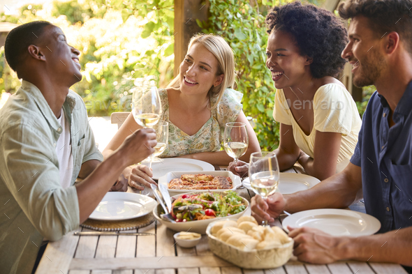 Group Of Smiling Multi-Cultural Friends Outdoors At Home Eating Meal And Drinking Wine Together - Stock Photo - Images