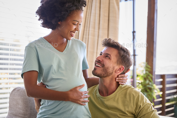 Multi-Racial Couple With Pregnant Woman In Bedroom At Home With Man Feeling Baby Kicking - Stock Photo - Images