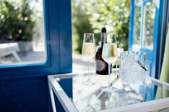 Close up of champagne glasses on transparent table. Bottle of wine and ice cooler.