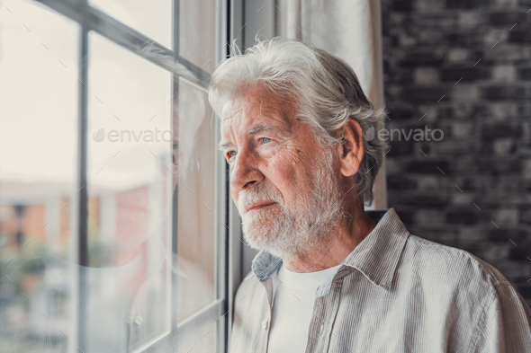 Pensive elderly mature senior man in eyeglasses looking in distance out of window