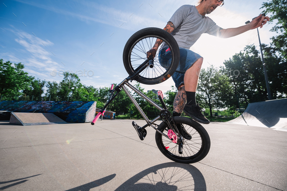 Wide-angle view of a professional mature bmx bike rider doing tricks in a skate park.