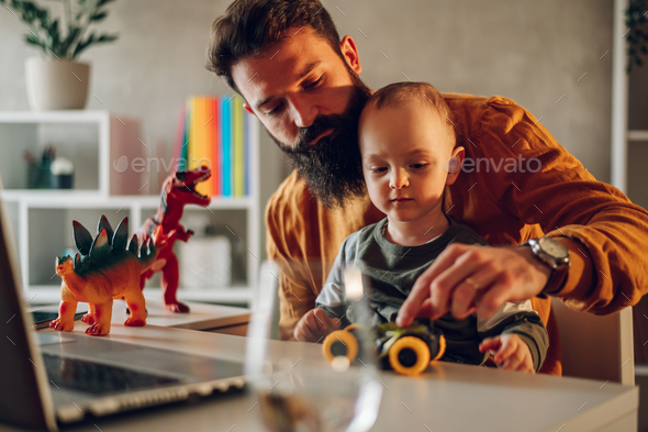 A casual remote businessman is sitting at the cozy home office with his son. - Stock Photo - Images