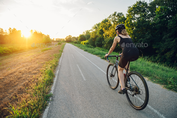 Rear view of a woman riding a bike during a sport cycling race outside of the city - Stock Photo - Images