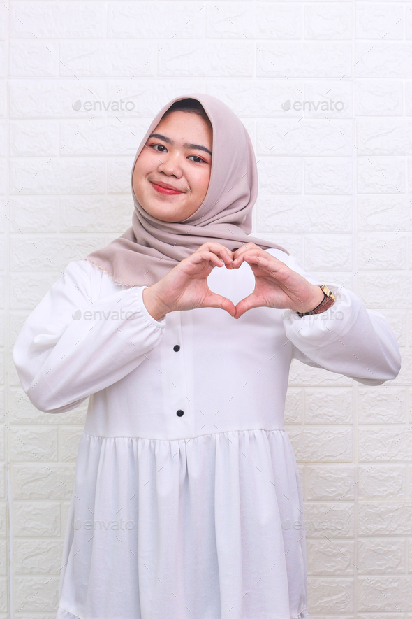 Asian muslim woman smiling confident showing hands sign of love  - Stock Photo - Images