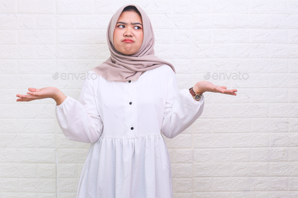 Doubtful Asian muslim woman having clueless and confused expression with arms and hands raised - Stock Photo - Images