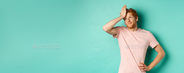 Annoyed and bothered redhead male model showing facepalm and roll eyes, standing over mint