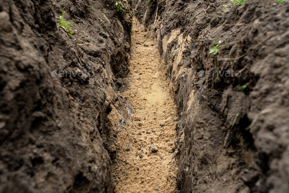 A trench dug in the yard along the fence to lay the drainage pipe,visible yellow sand. - Stock Photo - Images