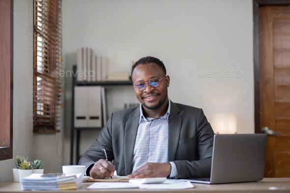 Handsome african american businessman in classic suit and eyeglasses is using a laptop and making - Stock Photo - Images