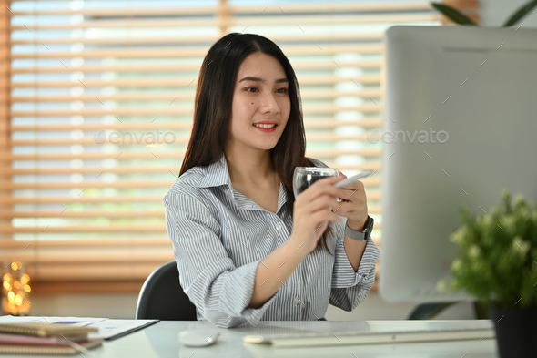 Pleasant asian female entrepreneur holding cup of coffee and reading business email laptop - Stock Photo - Images